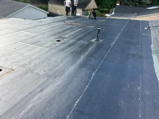 Flat roof with dark membrane material, sealed seams, and metal flashing penetration
