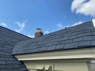 Dark gray slate roof with brick chimney and cream siding trim