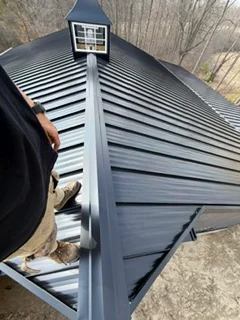 Standing seam metal roof installation with charcoal gray panels and roof vent