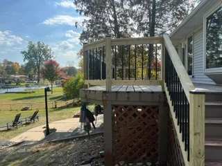 Elevated wooden deck with pergola, lattice skirting, and black railings attached to house