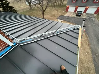 Standing seam metal roof installation with white trim and horizontal panels
