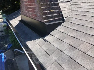 Metal roof flashing installed around brick chimney with new gutter system on asphalt shingle roof