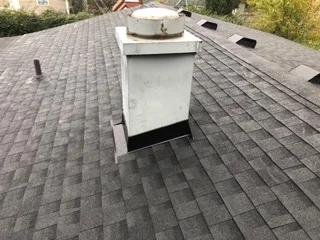 Gray asphalt shingle roof with white metal chimney chase and flashing installed