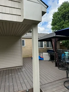 Gray composite deck with vinyl siding and white support posts on residential home