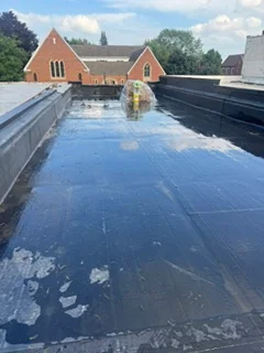 Dark membrane flat roof waterproofing with perimeter flashing on commercial building