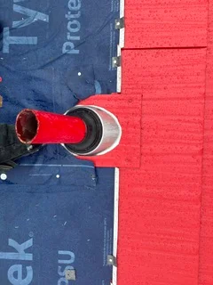 Red metal roof flashing boot around ventilation pipe with blue underlayment visible