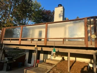Elevated residential deck with metal railings, translucent panels, and new siding installation