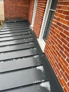 Dark flat roof membrane with metal flashing installed against brick walls
