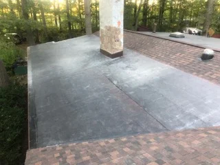 Concrete patio with brick paver border and central support column in wooded setting