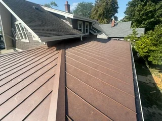Standing seam metal roof installation with brown panels and chimney flashing