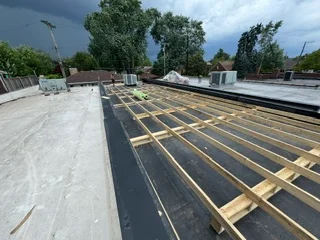Flat roof framing with wooden joists and black membrane underlayment installation