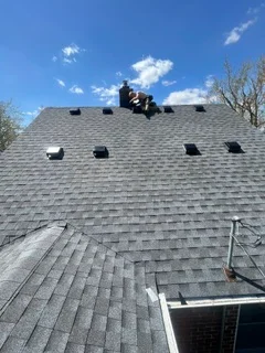 Gray asphalt shingles installed on residential roof with ventilation pipes and guttering