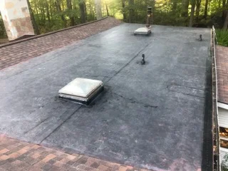 Dark membrane flat roof with two skylights and brick paver border