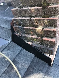 New black flashing installed at chimney base meeting asphalt shingle roof