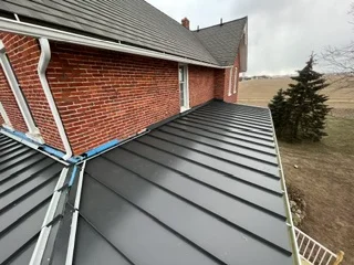 Standing seam metal roof with charcoal panels and chimney flashing on brick home
