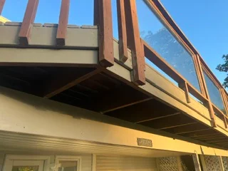 Wooden deck with exposed beams, vertical posts, and railing system under clear sky