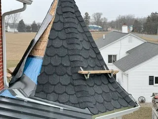 Steep conical roof with new dark asphalt shingles and metal guttering installed