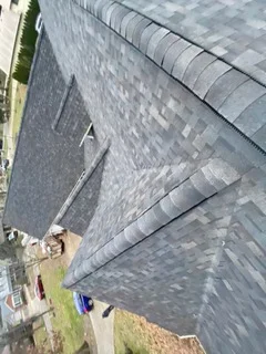Newly installed gray asphalt shingles with ridge cap on residential roof